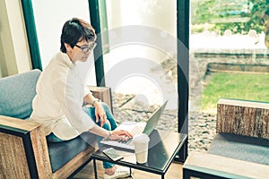 Asian mature woman using laptop with smartphone and coffee at cafe, vintage tone, middle aged adult with modern gadget technology