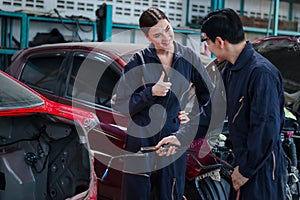 Asian mechanic man in uniform welding car body panel vehicle, beautiful woman technician coworker giving thump up, auto mechanic