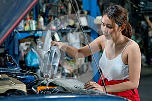 Asian mechanic woman take care engine of car by filling some chemical in the front of car and work in garage workplace