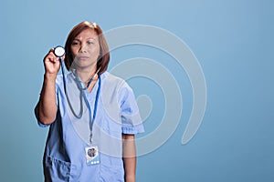 Asian medical assistant wearing blue uniform during checkup visit holding stethoscope