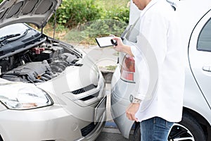 Asian men driver check for damage after a car accident before taking pictures and sending insurance. Online car accident insurance