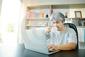 Asian men work at home in the office. Drinking coffee and typing in computer notebooks.