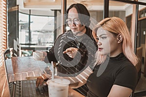 An asian mentor or supervisor instructs and teaches a younger asian woman protege on computer work. Casual scene at a coworking photo
