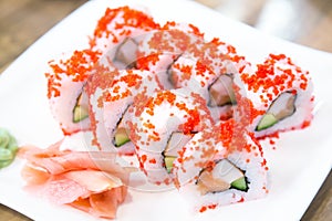 Asian menu. Californian sushi rolls with Masago caviar near ginger and wasabi on white plate. Japanese cuisine. Close up image.