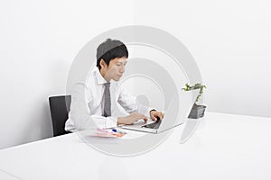 Asian mid adult businessman using laptop at desk in office