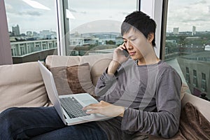 Asian mid adult man on call while using laptop in living room