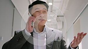 Asian middle-aged businessman adult entrepreneur in office hallway talk mobile phone negotiate by smartphone smiling