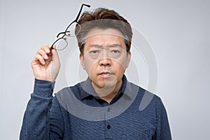 Asian middle-aged male trying to take off glasses and see something. poor sight, presbyopia, myopia photo