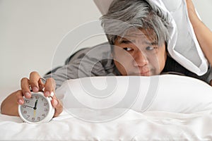 Asian middle-aged man is holding a white alarm clock and his face showed boredom and feeling bad, his problem is a sleep disorder.