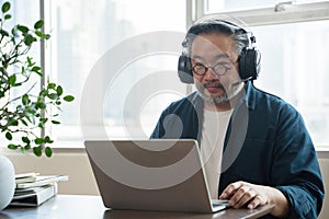 Asian middle aged man sitting at home working on video call. Work from home concept.