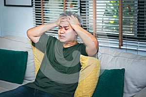 Asian middle-aged man, sitting on the sofa, He is a headache and stress