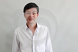 Asian middle-aged man in white shirt smiling and looking at camera on grey background, authentic half body portrait. Happy people