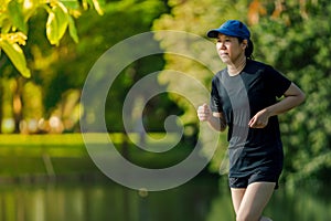 Asian middle-aged woman wearing a black dress, blue hat, running stretching in park near to lake. Get the sun light in the morning