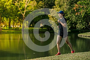 Asian middle-aged woman wearing a black dress, blue hat, running stretching in park near to lake. Get the sun light in the morning