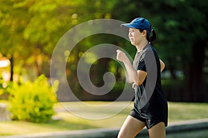 Asian middle-aged woman wearing a black dress, blue hat, running stretching in park near to lake. Get the sun light in the morning