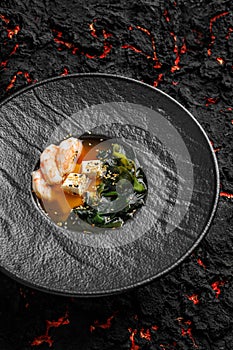 Asian miso soup ,soy sauce, greens and shrimps prawn. On a black stone background