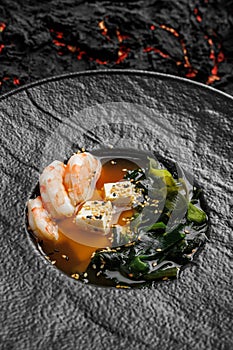 Asian miso soup ,soy sauce, greens and shrimps prawn. On a black stone background, macro