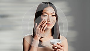 Asian model applying facial anti aging cream on cheeks