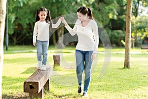 Asian mom and cute baby kid holding hand playing together at wood log walk in nature park outdoor playground in casual white blue