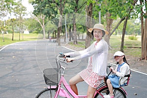 Asian mom and daughter riding bicycle together in park. Happy family