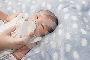 Asian mom feeding bottle of milk to Newborn baby cute son in a bedroom