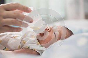 Asian mom feeding bottle of milk to Newborn baby cute son in a bedroom