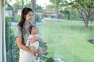 Asian mom holding her baby newborn in hand and looking nature outside window sweet and lovely.Good moment of Happy mother and