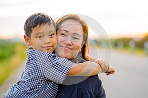 Asian mom hug her young son lovingly at sunset with nature background