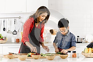 Asian mom in red shirt and black apron is teaching her son