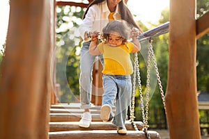 Asian Mommy With Baby Walking Swinging Bridge At Playground Outdoor