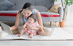 Asian mother and 7 month old daughter sitting on the floor and looking at a tablet