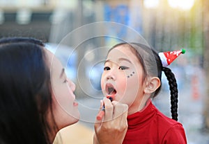 Asian mother applying lipstick over daughter mouth
