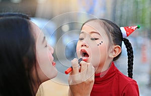 Asian mother applying lipstick over daughter mouth