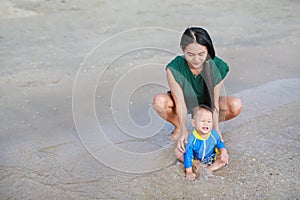 Asian mother and baby boy playing water on beach