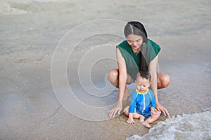 Asian mother and baby boy playing water on beach