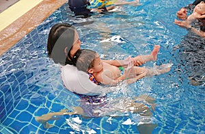 Asian mother and baby boy swimming in pool training with happiness
