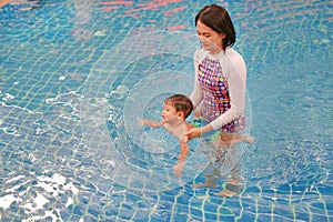 Asian mother and baby boy swimming in pool training with happiness