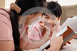 Asian mother and boy, wearing a pink t-shirt, The two of them lay comfortably on the bed, mother holding a playbook in her hand to