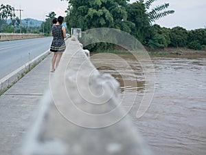 Asian mother carrying her little daughter standing on a bridge showing her little baby a murky muddy river aft