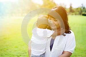 Asian mother carrying and holding her son in green park sunlight