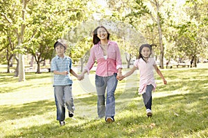 Asian mother and children running hand in hand in park