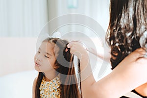 Asian mother combing hair daughter in bed