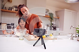 Asian Mother And Daughter Baking Cupcakes In Kitchen At Home Whilst On Vlogging On Mobile Phone photo