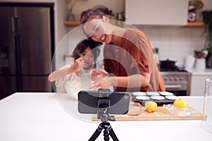 Asian Mother And Daughter Baking Cupcakes In Kitchen At Home Whilst On Vlogging On Mobile Phone photo