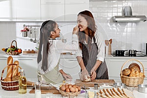 Asian Mother and daughter happily bake. The daughter teased her mother to bring the powder on her face at the kitchen in the house