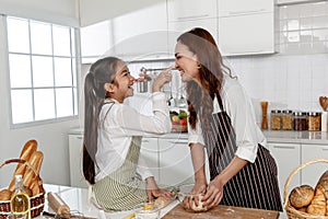 Asian Mother and daughter happily bake. The daughter teased her mother to bring the powder on her face at the kitchen in the house