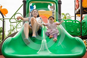 Asian mother and daughter are happiness and enjoy playing slide equipment together in playground, with fully happiness moment