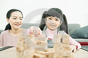 Asian mother and daughter playing wood block tower stacking game in cozy modern home. Ethnic babysitter engaging little girl in