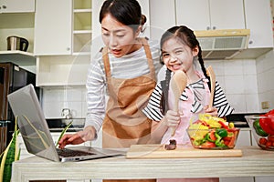 Asian mother and daughter preparing salad and using computer notebook. Leisure activity in a kitchen