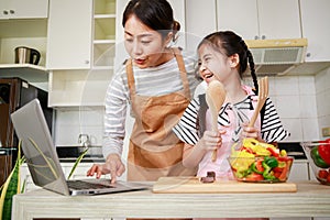 Asian mother and daughter preparing salad and using online method from computer notebook